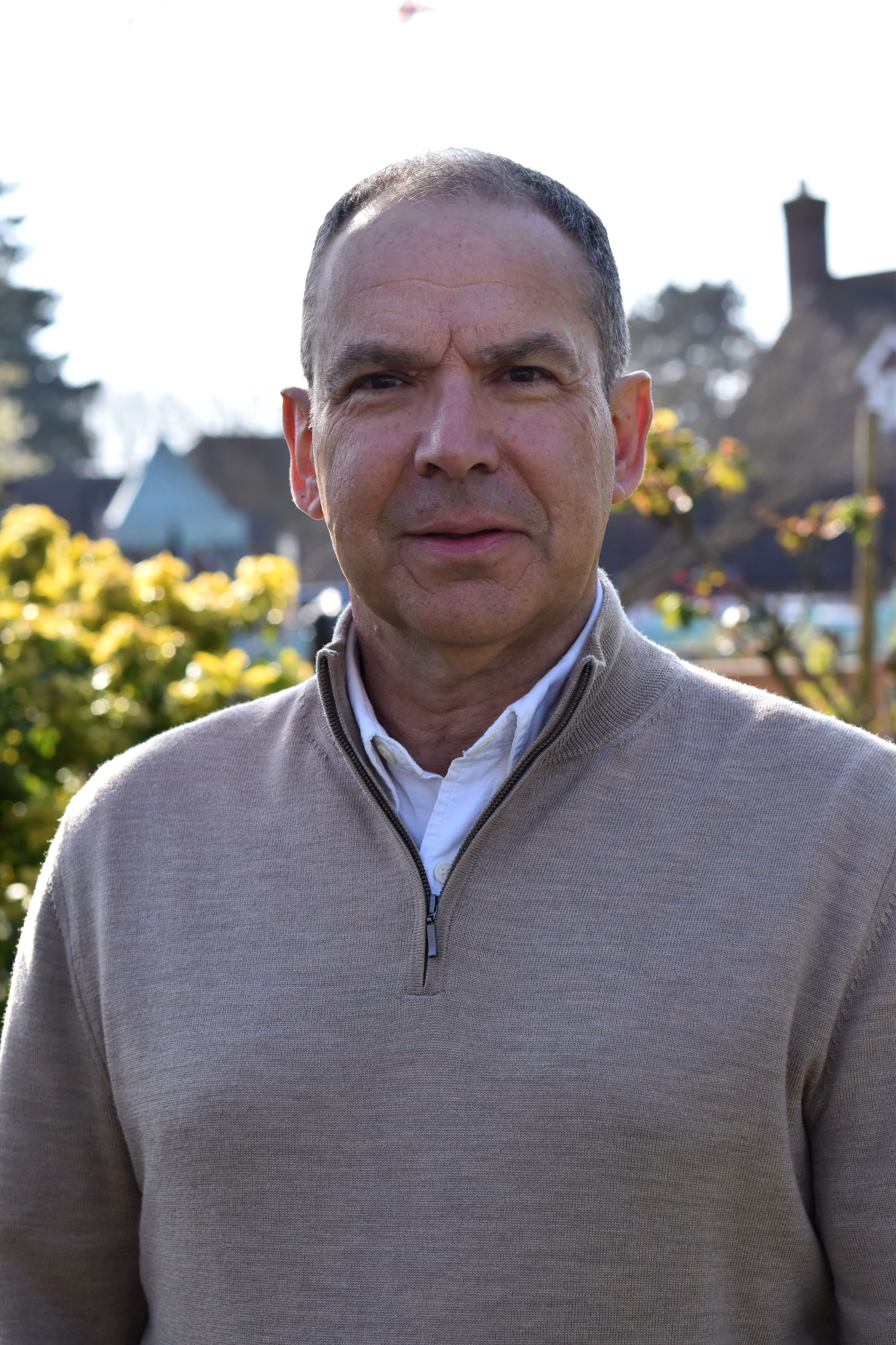 Chair of Investment Committee Paul Hewish stands in sunny gardens, wearing a beige zip top jumper.