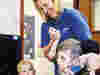 A Demelza nurse smiling while holding hands of a young child in a chair