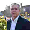 Trustee Paul Smith stands in sunny gardens wearing a white shirt and navy blue blazer.