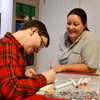 A child drawing at a table with a Demelza Health Care Assistant 