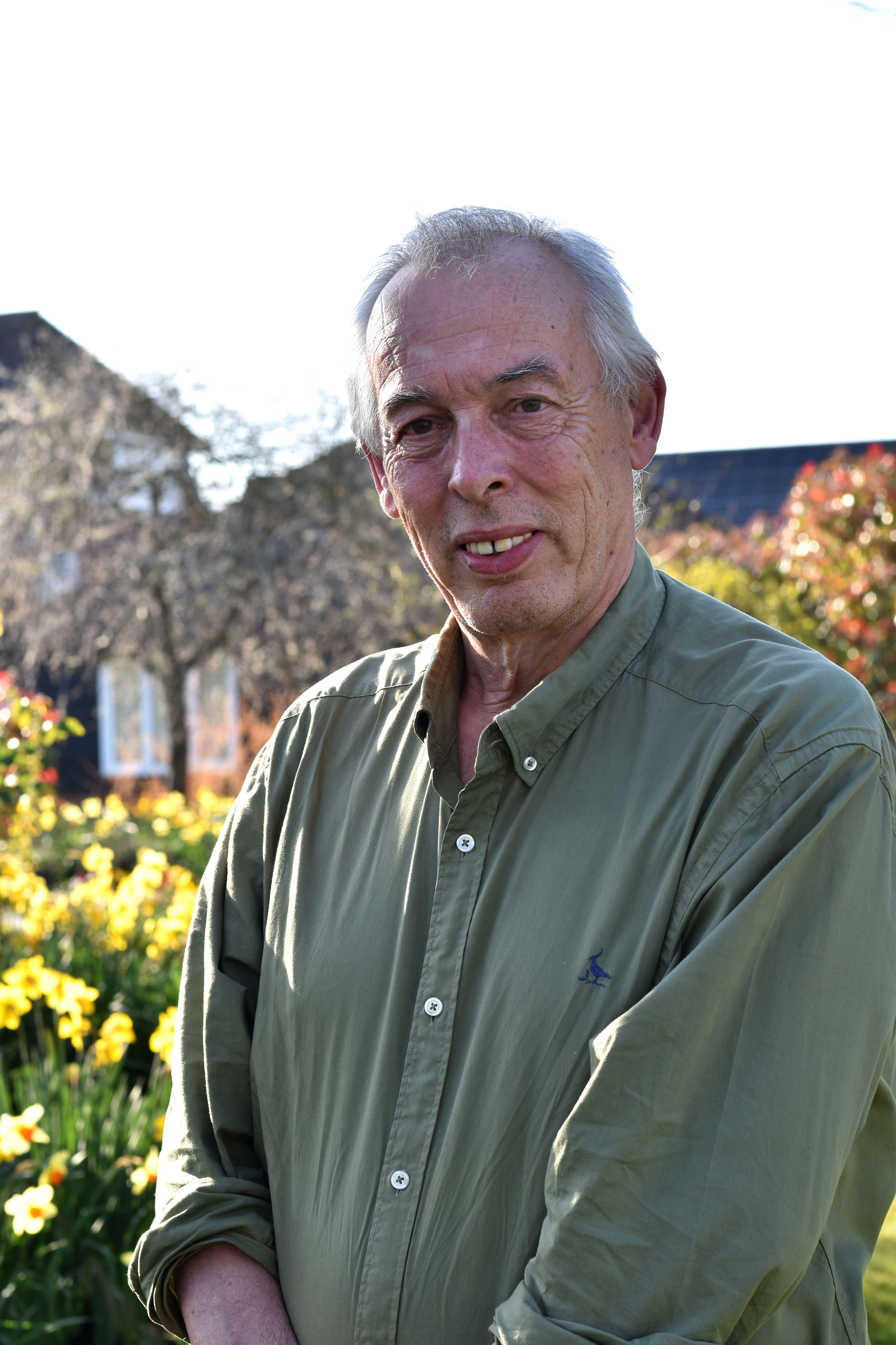 Sir Richard Douglas stands in sunny gardens, wearing a green khaki shirt.
