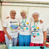 Three volunteers in bright clothes stand behind a table in a white marquee at the Mote Park Bubble Rush 2025 event.