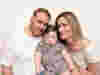 A man with brown hair and a woman with blonde hair holding a young boy smiling