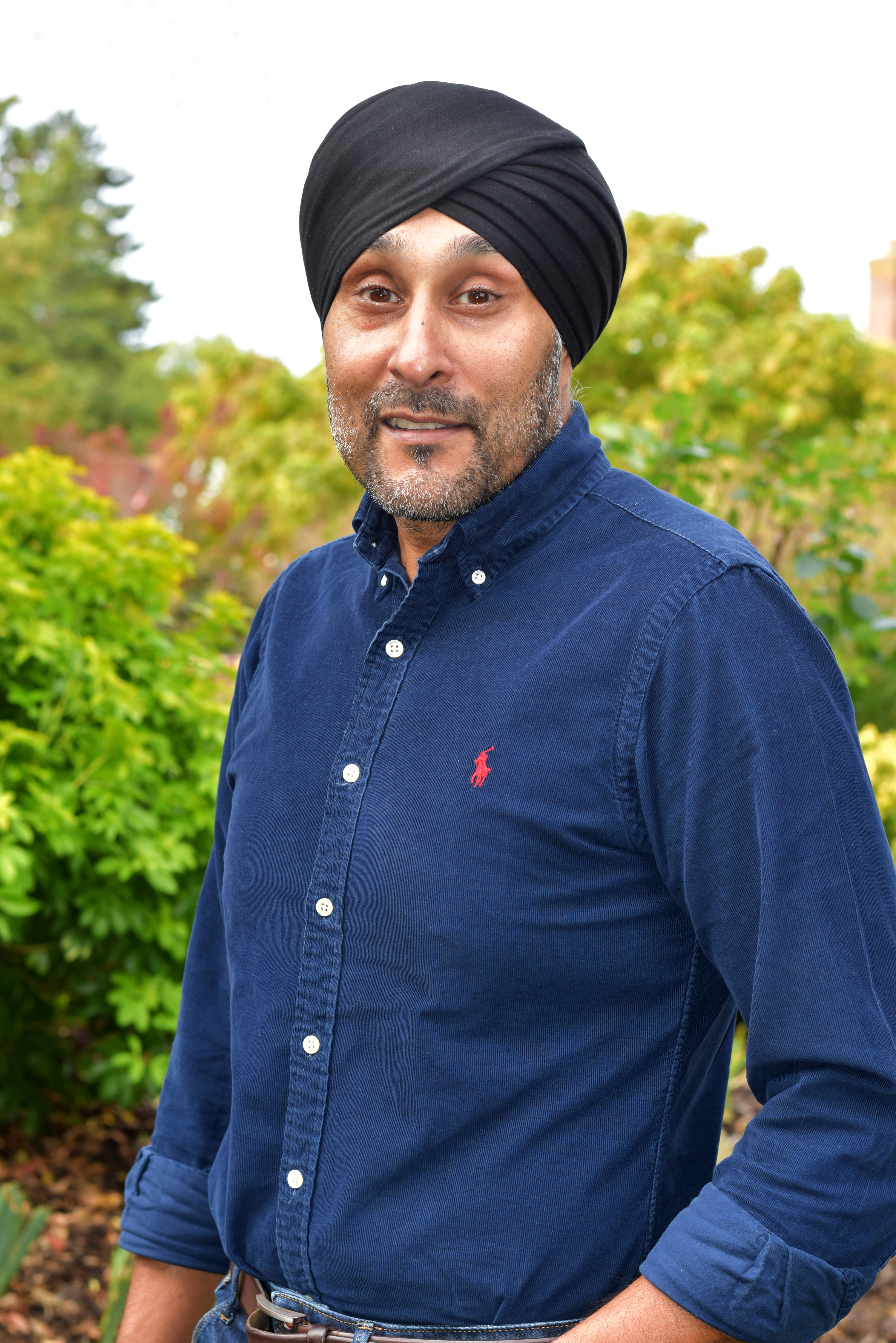 Trustee Ziggie Singh standing in a garden, wearing a black turban and a smart navy blue shirt.
