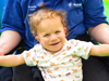 A child with curly hair smiling to the camera with a Demelza nurse