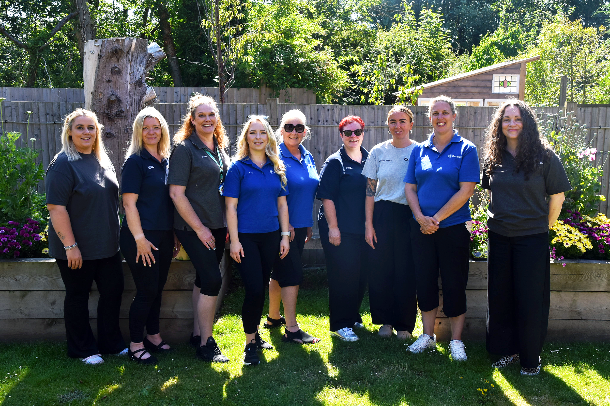 Nine female East Sussex team members stand side by side in a garden on a sunny day, smiling.