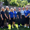 Nine female East Sussex team members stand side by side in a garden on a sunny day, smiling.