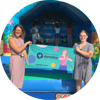 Two women holding up a Demelza banner infront of a bouncy castle