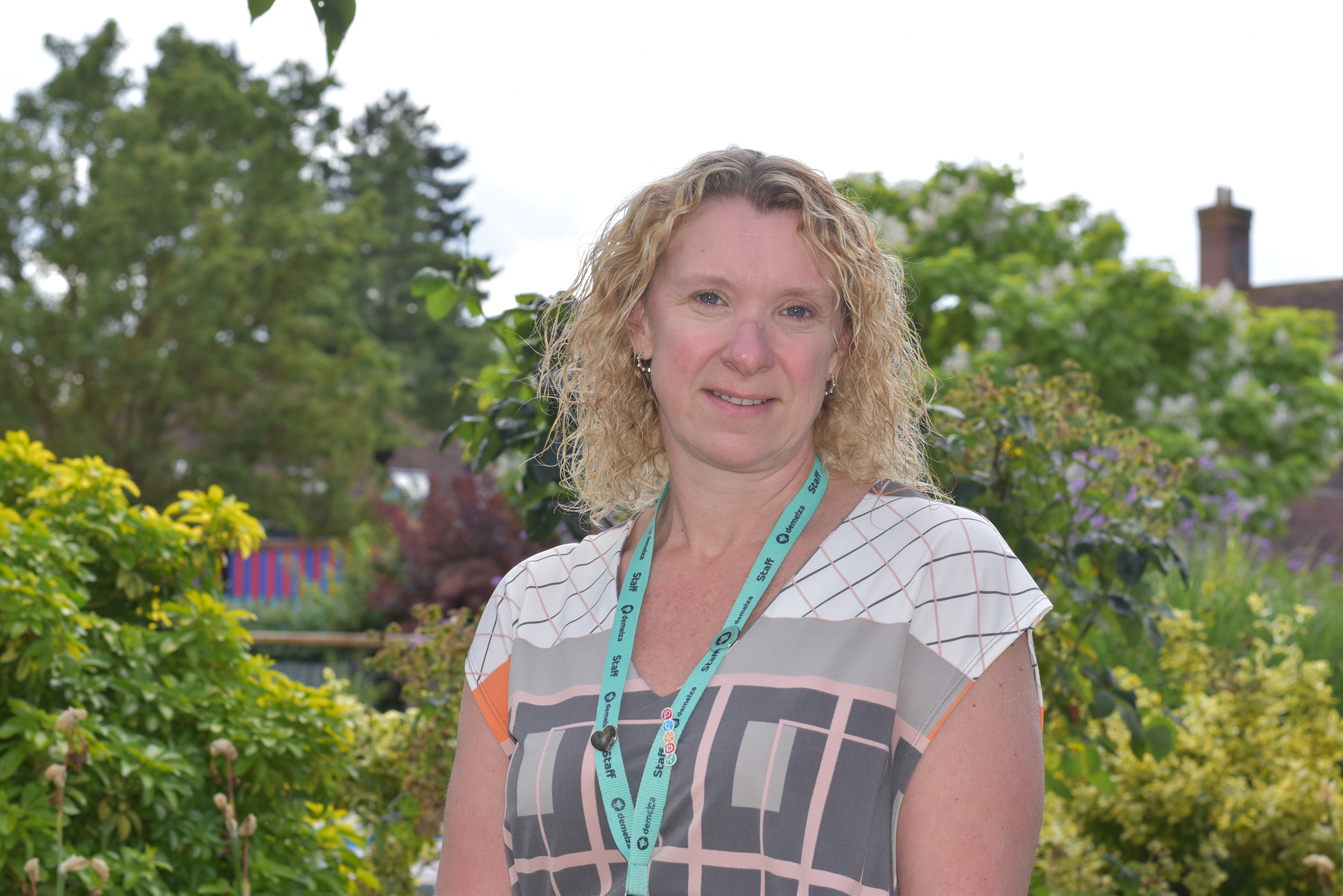 Charlotte Chamberlain, Director of Finance and Resources, stands smiling in Demelza’s hospice gardens wearing a patterned top.