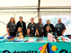 Demelza staff members stand and sit behind two branded tables at Family Discovery Day 2025, smiling and greeting visitors.