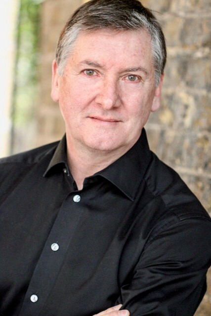 Headshot of Robin Cousins, Demelza celebrity ambassador, wearing a black shirt and looking directly at the camera 