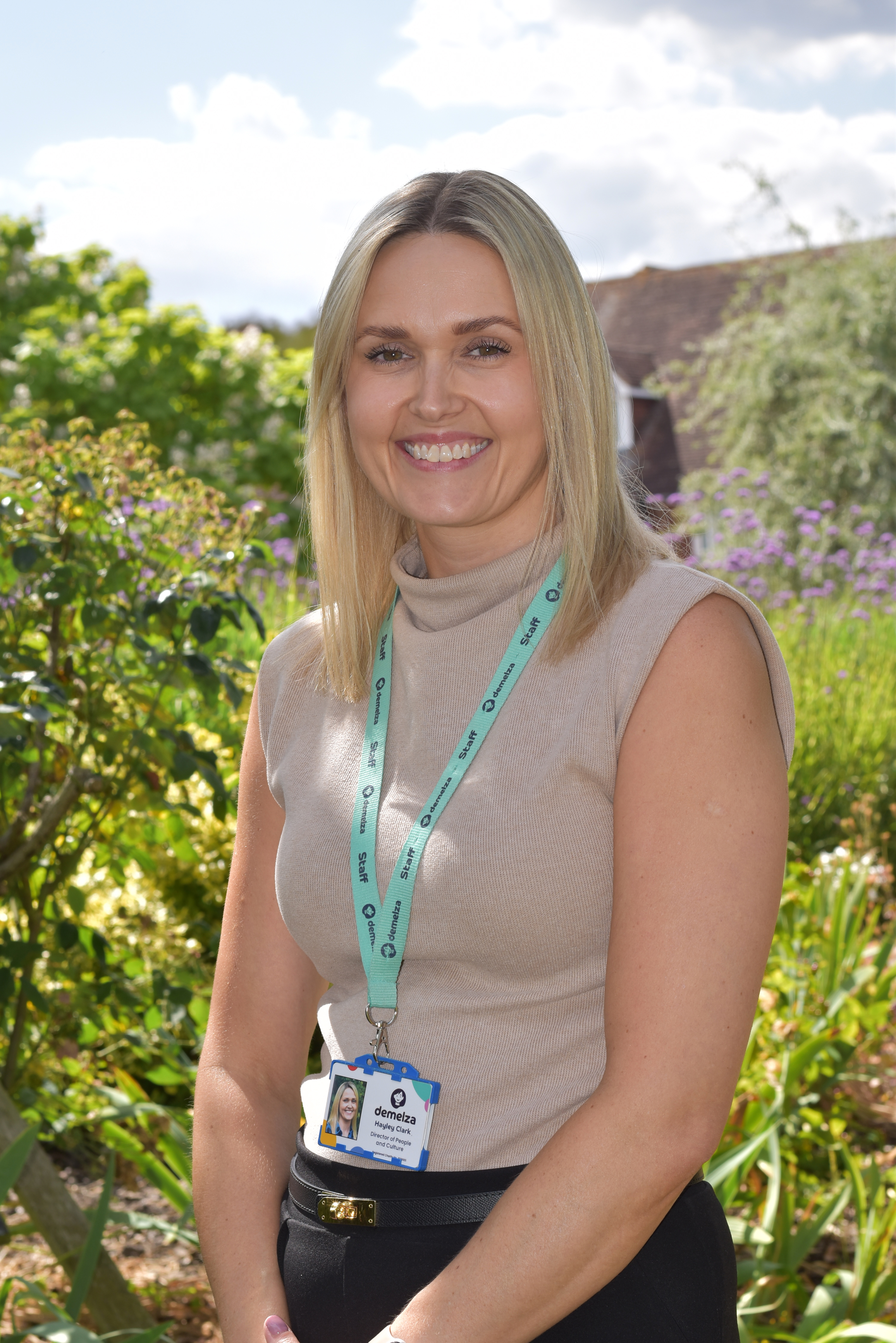 Hayley Clark, Director of People and Culture, stands smiling in Demelza’s hospice gardens wearing a smart beige roll neck top.