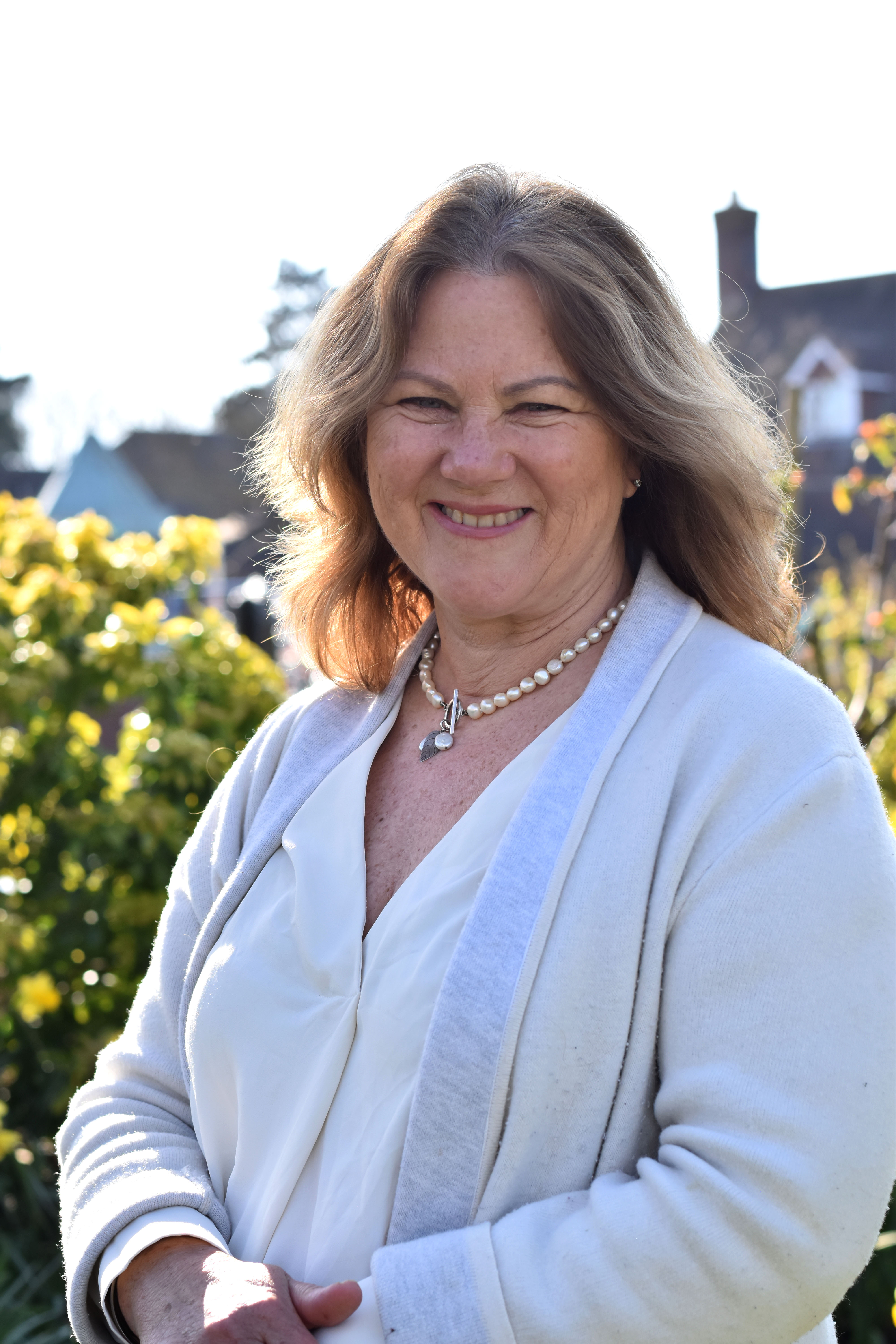 Trustee Susan Tether smiles in sunny gardens, wearing a cream outfit and pearl necklace.
