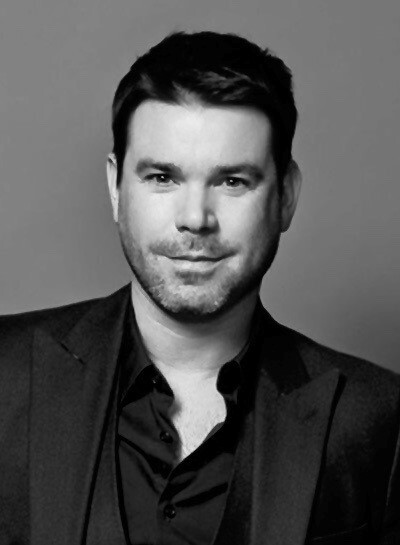 Headshot of Dave Berry, Demelza celebrity ambassador, smiling in a smart black suit and shirt.