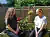 Two female Care Team staff members sitting outdoors in the sunny East Sussex gardens, surrounded by blooming flowers.