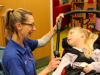 A nurse with glasses smiling towards a child in a wheelchair