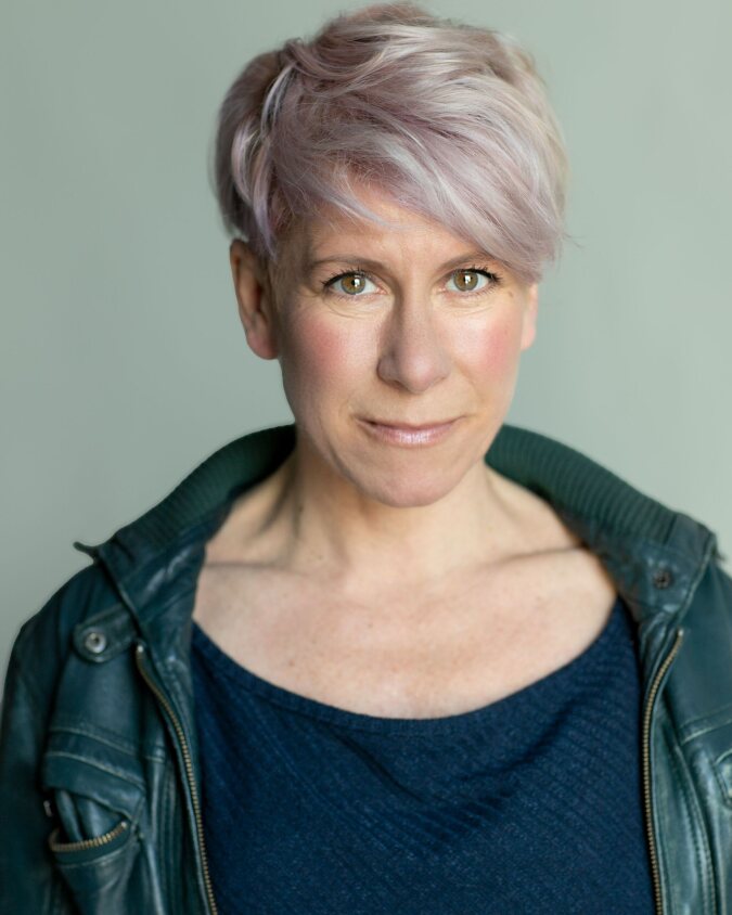 Headshot of Anna-Jane Casey, Demelza celebrity ambassador, wearing a blue top and green leather jacket with short cropped light hair.