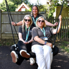 Three East Sussex family engagement team members sit on a swing in a sunny garden, smiling.
