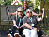 Three East Sussex family engagement team members sit on a swing in a sunny garden, smiling.